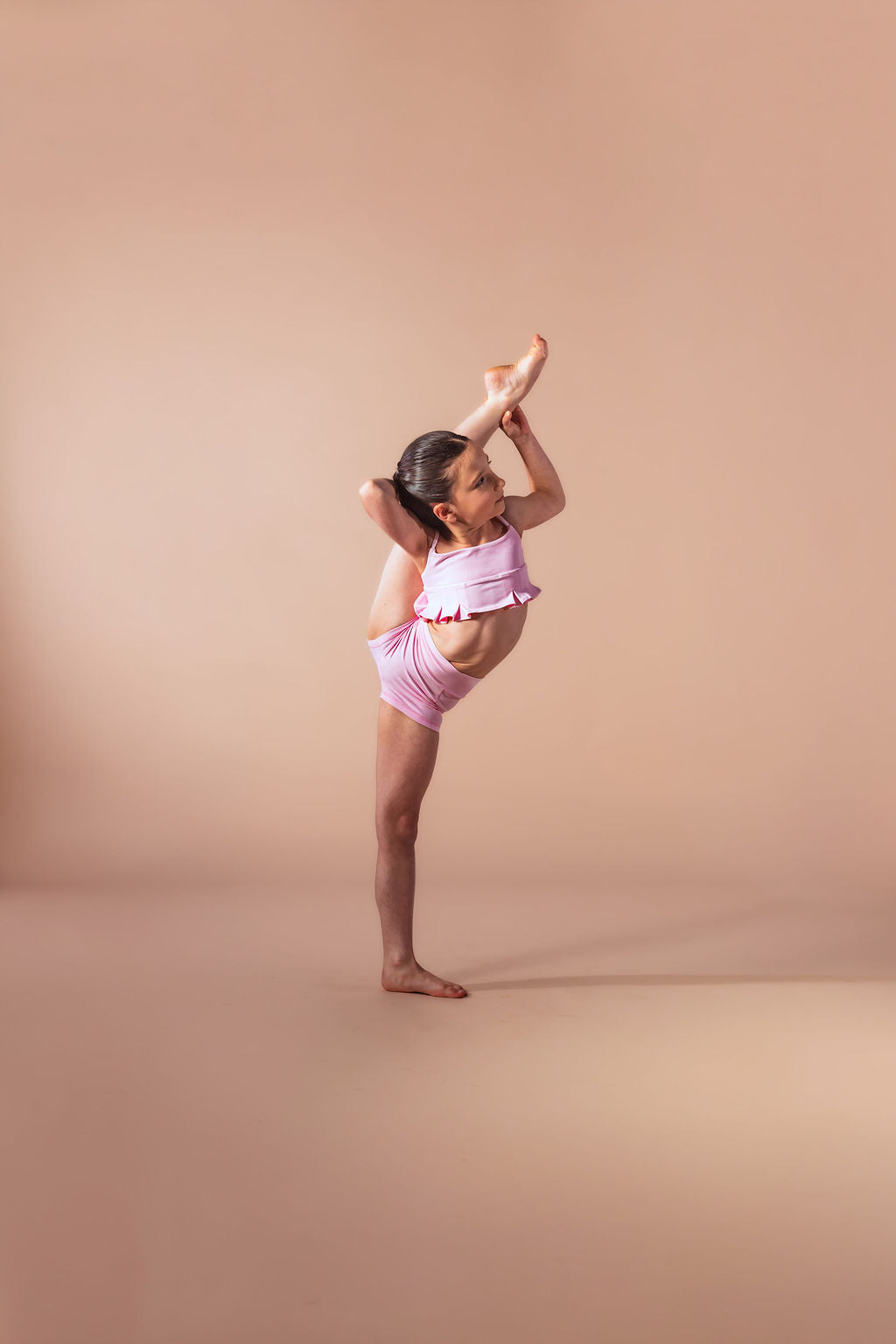 Young dancer in a pink outfit performing a pose on a beige background