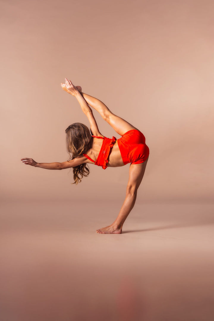 Dancer in a red outfit performing a pose on a beige background