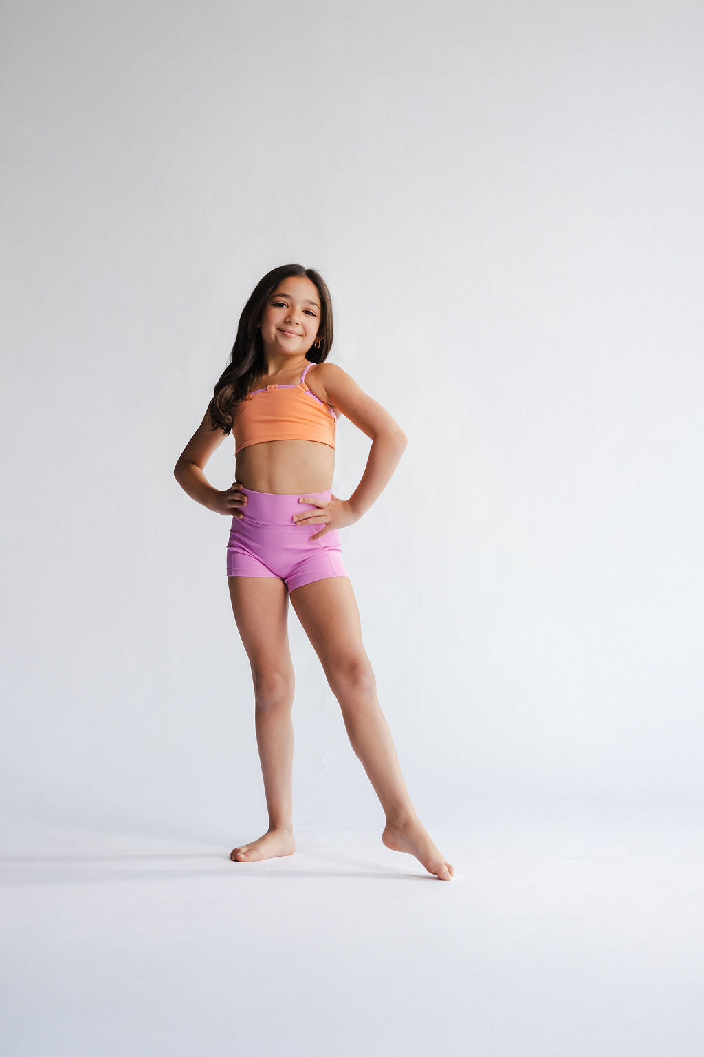 Young girl in a sports bra and shorts posing on a white background