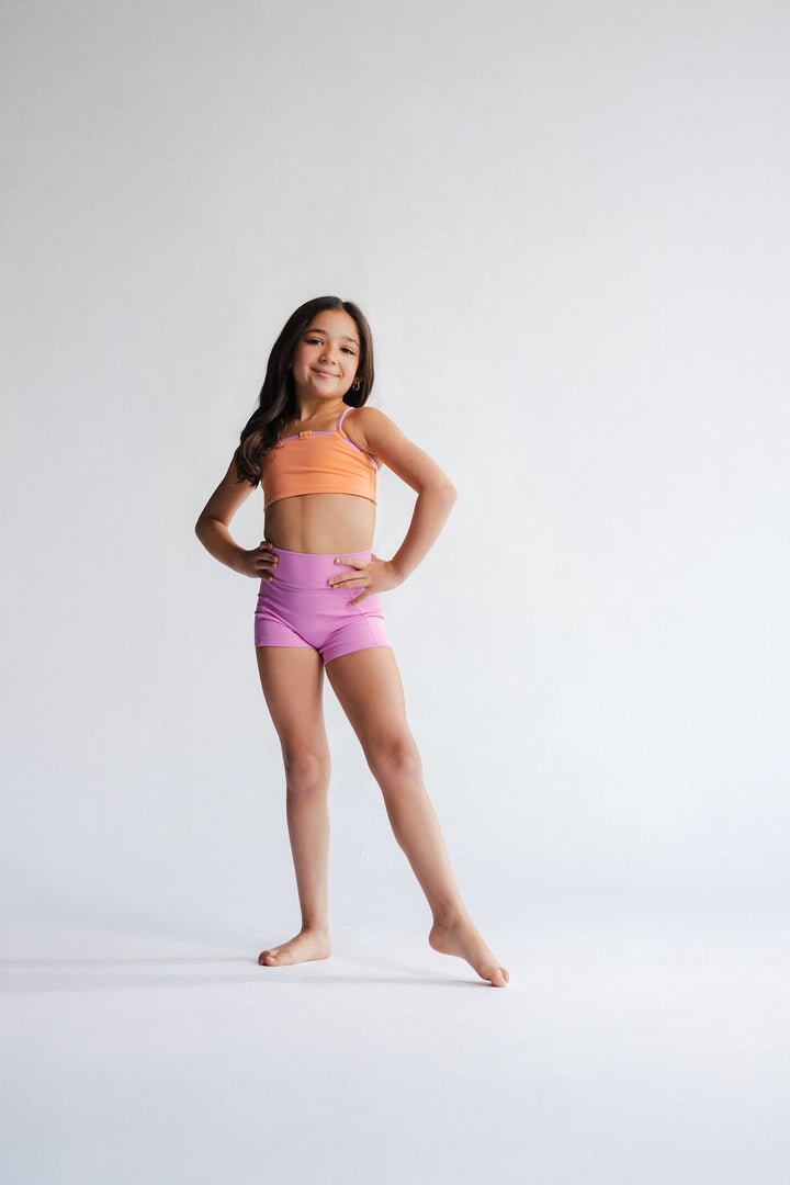 Young girl in a sports bra and shorts posing on a white background