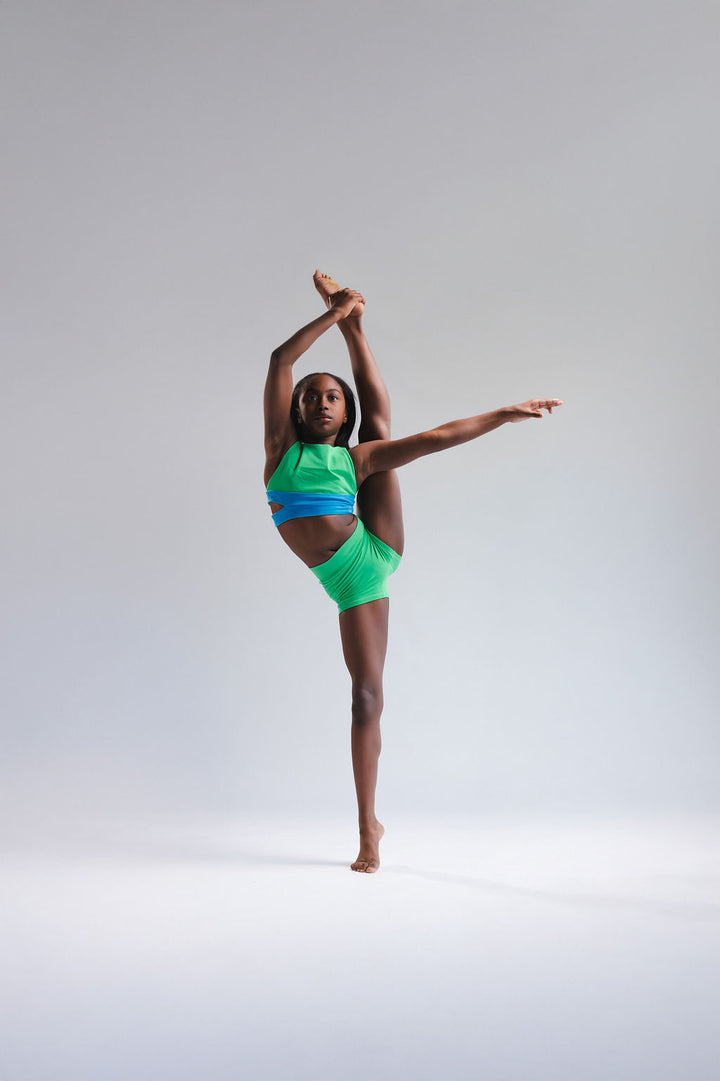 Person in green and blue athletic wear performing a yoga pose on a gray background
