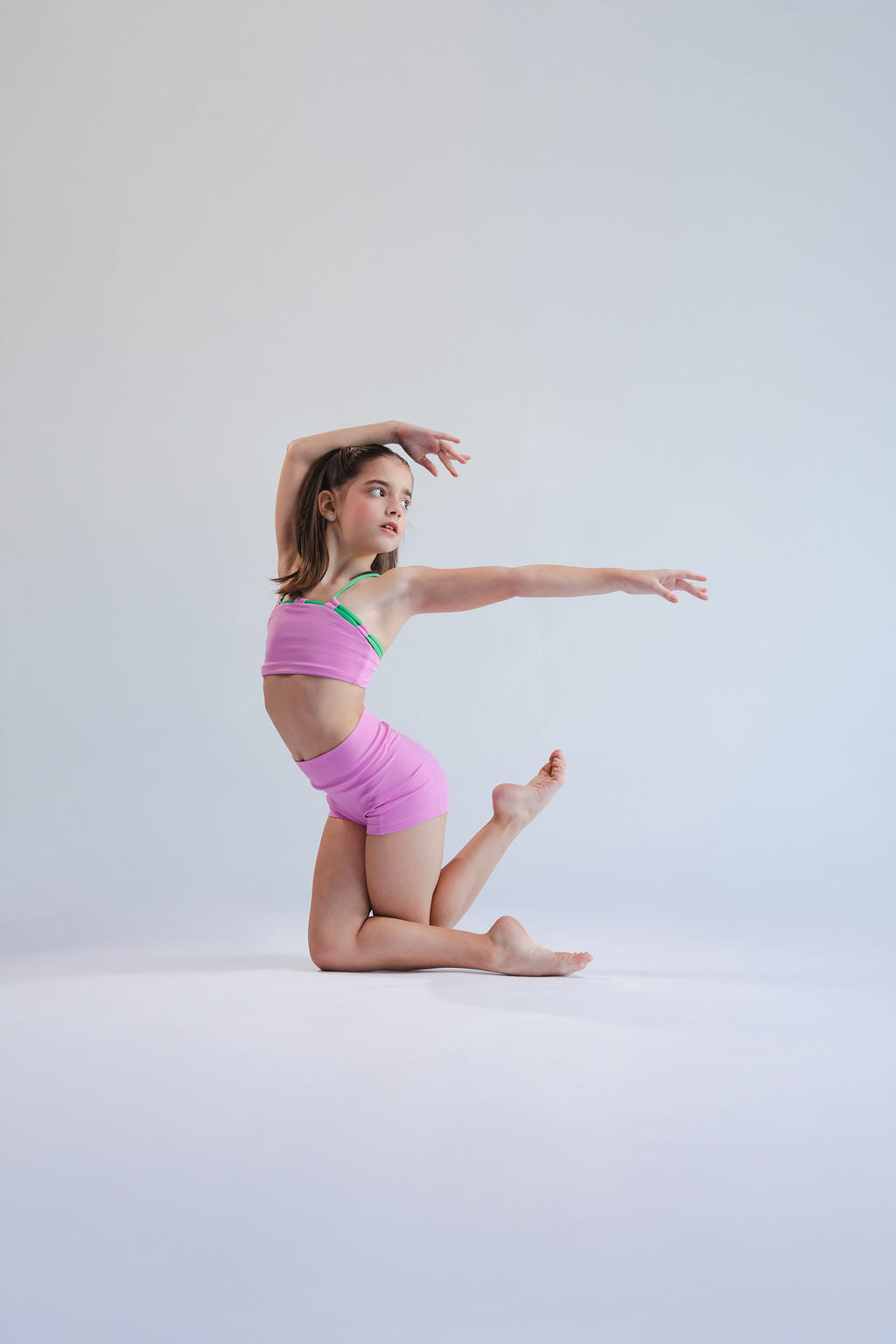 Young girl in a pink outfit posing on a light gray background