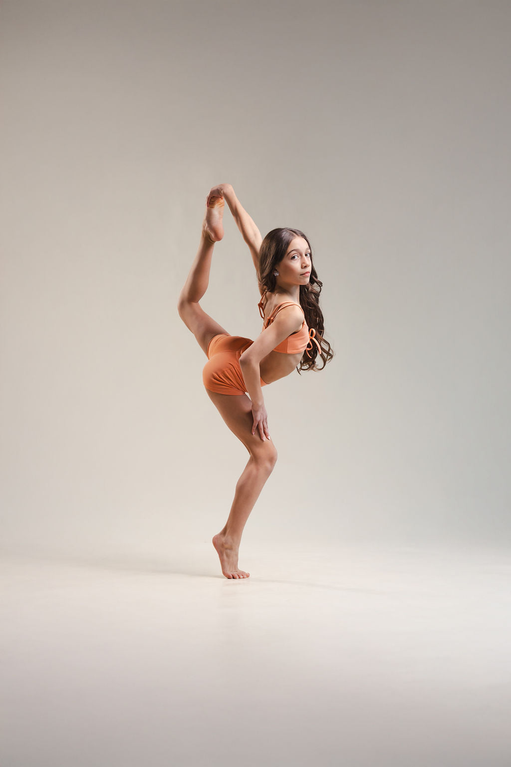 Dancer in orange outfit performing a pose on a plain background