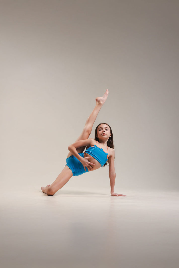 Dancer in a blue outfit performing a pose on a plain background