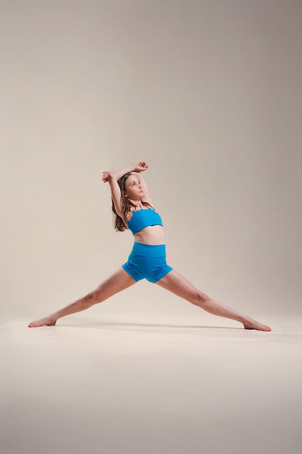 Woman in blue athletic wear performing a dance pose on a beige background