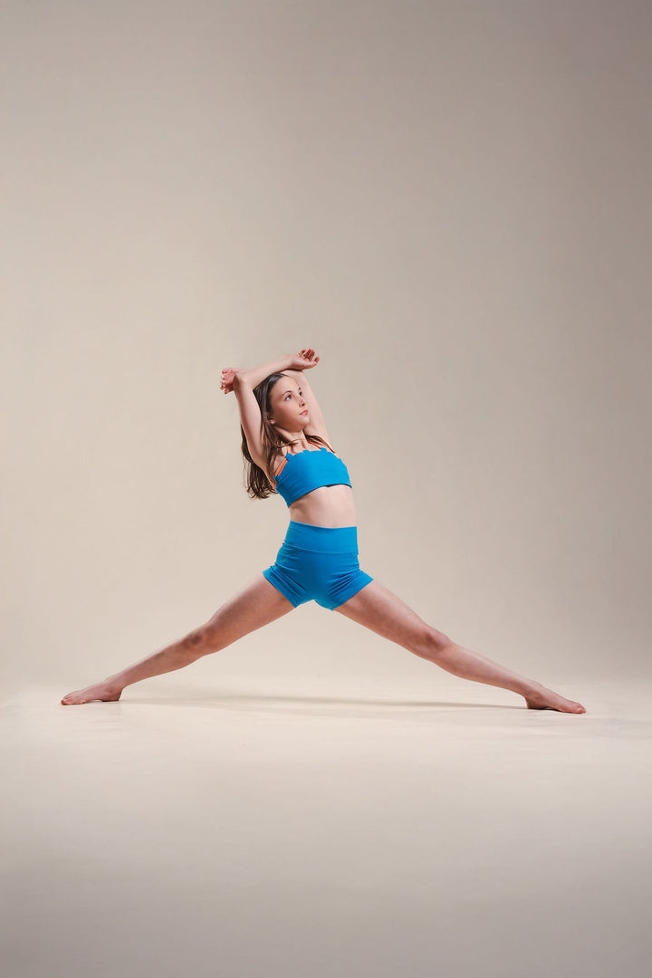 Woman in blue athletic wear performing a dance pose on a beige background