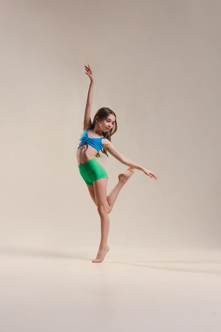 Dancer in a blue top and green shorts posing on a beige background