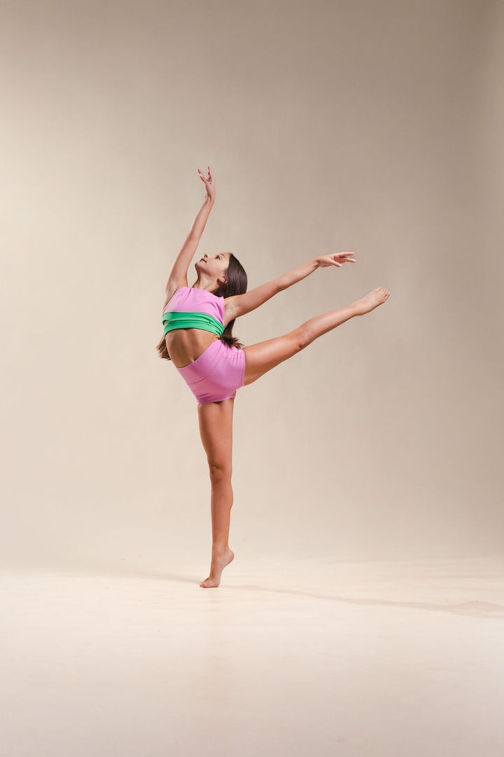 Dancer in a pink and green outfit performing a pose on a beige background