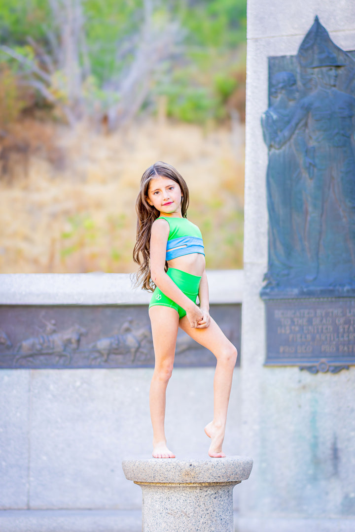 Young girl in green swimsuit standing on a stone pedestal with a scenic background